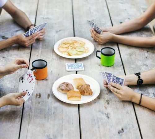 Close up of four people sitting at a table, playing cards.