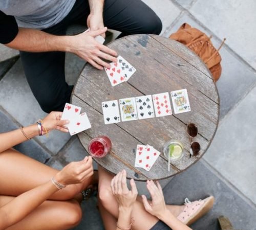Young friends playing poker card game at cafe